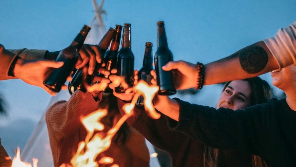 groupe d'amis qui trinquent avec bières devant un feu - Photo de Pexels by Kindel Media